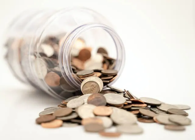 Tarro de monedas volcado sobre una superficie blanca